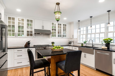 Inspiration for an u-shaped light wood floor kitchen remodel in Minneapolis with white cabinets, white backsplash, subway tile backsplash, stainless steel appliances, an island and black countertops