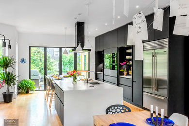 Inspiration for a large modern single-wall light wood floor and beige floor eat-in kitchen remodel in Boston with an undermount sink, flat-panel cabinets, black cabinets, concrete countertops, black backsplash, window backsplash, stainless steel appliances and an island