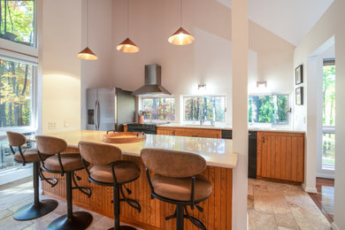 Inspiration for a large 1960s travertine floor and vaulted ceiling kitchen remodel in New York with an undermount sink, medium tone wood cabinets, quartz countertops, stainless steel appliances, an island and white countertops