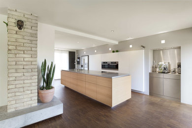 This is an example of a contemporary kitchen in Other with flat-panel cabinets, medium wood cabinets, solid surface benchtops, stainless steel appliances, with island, brown floor and grey benchtop.