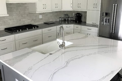 Large transitional l-shaped medium tone wood floor and brown floor eat-in kitchen photo in Other with an undermount sink, recessed-panel cabinets, white cabinets, quartz countertops, gray backsplash, stone tile backsplash, stainless steel appliances and an island