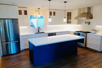 Large arts and crafts l-shaped light wood floor and beige floor eat-in kitchen photo in Sacramento with a farmhouse sink, shaker cabinets, white cabinets, quartz countertops, white backsplash, quartz backsplash, stainless steel appliances, an island and white countertops
