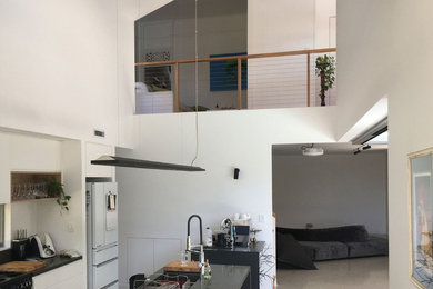 Large traditional galley open plan kitchen in Brisbane with white cabinets, granite benchtops, concrete floors, multiple islands and black benchtop.