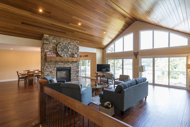 Photo of a mid-sized country open concept living room in Toronto with yellow walls, dark hardwood floors, a two-sided fireplace, a stone fireplace surround, a freestanding tv and brown floor.