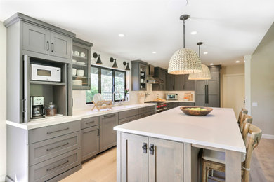 Mid-sized transitional l-shaped laminate floor open concept kitchen photo in Other with a double-bowl sink, flat-panel cabinets, gray cabinets, quartz countertops, white backsplash, ceramic backsplash, stainless steel appliances, an island and white countertops
