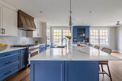 Example of a mid-sized classic medium tone wood floor eat-in kitchen design in Chicago with an undermount sink, blue cabinets, quartz countertops, glass tile backsplash, stainless steel appliances and an island