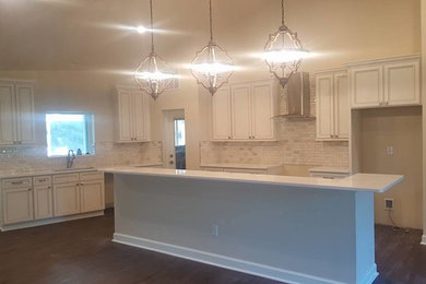 Open concept kitchen - large l-shaped laminate floor and brown floor open concept kitchen idea in Tampa with an undermount sink, recessed-panel cabinets, white cabinets, quartz countertops, white backsplash, glass tile backsplash, stainless steel appliances and an island