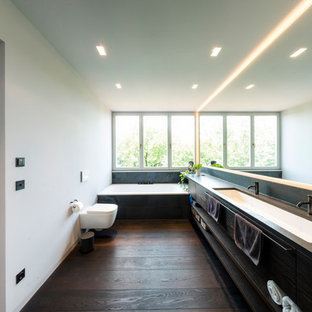 Foto di un'ampia stanza da bagno con doccia minimalista con ante lisce, vasca da incasso, WC sospeso, pareti grigie, pavimento in legno massello medio, top in superficie solida, pavimento marrone, ante in legno bruno, piastrelle nere, lavabo integrato e top marrone