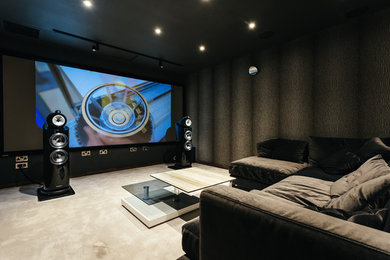 Medium sized contemporary enclosed home cinema in Cornwall with black walls, carpet, a projector screen and beige floors.