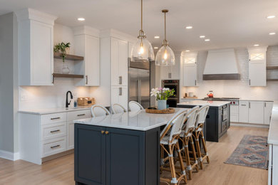 Eat-in kitchen - huge transitional galley light wood floor and gray floor eat-in kitchen idea in Other with a farmhouse sink, recessed-panel cabinets, white cabinets, quartz countertops, white backsplash, subway tile backsplash, stainless steel appliances, two islands and white countertops