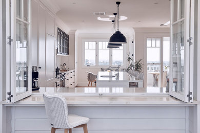 Inspiration for a large beach style galley kitchen in Sydney with an undermount sink, recessed-panel cabinets, white cabinets, white splashback, panelled appliances, medium hardwood floors, with island, brown floor and white benchtop.