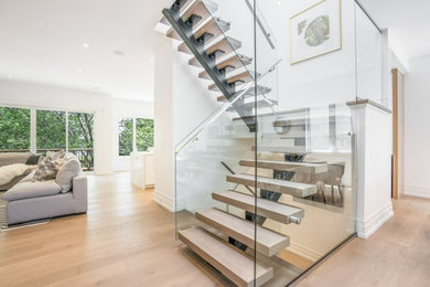 Imagen de escalera en U contemporánea de tamaño medio con escalones de madera, contrahuellas de metal y barandilla de vidrio