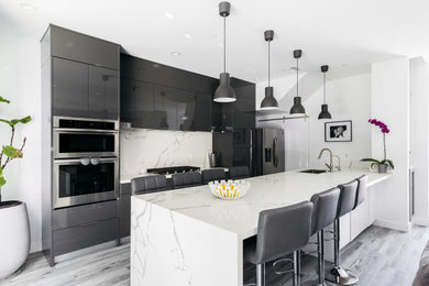 Minimalist galley vinyl floor and gray floor eat-in kitchen photo in Los Angeles with a double-bowl sink, flat-panel cabinets, gray cabinets, quartz countertops, white backsplash, quartz backsplash, stainless steel appliances, an island and white countertops