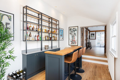 Inspiration for a medium sized urban galley breakfast bar in Hertfordshire with shaker cabinets, black cabinets, engineered stone countertops, medium hardwood flooring, brown floors, grey worktops and a feature wall.