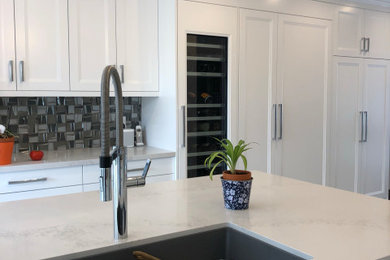Transitional enclosed kitchen photo with an undermount sink, recessed-panel cabinets, white cabinets, quartzite countertops, gray backsplash, paneled appliances, an island and white countertops