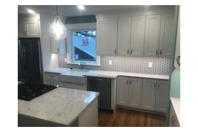 Mid-sized elegant light wood floor and brown floor eat-in kitchen photo in Other with a farmhouse sink, shaker cabinets, white cabinets, quartz countertops, gray backsplash, ceramic backsplash, stainless steel appliances, an island and white countertops