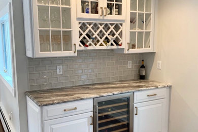 Small transitional single-wall medium tone wood floor and brown floor home bar photo in Other with raised-panel cabinets, white cabinets, granite countertops, glass tile backsplash and gray countertops