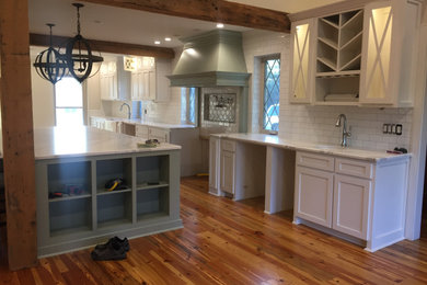 Eat-in kitchen - large cottage single-wall medium tone wood floor and exposed beam eat-in kitchen idea with an undermount sink, shaker cabinets, white cabinets, quartz countertops, white backsplash, subway tile backsplash, stainless steel appliances, two islands and white countertops