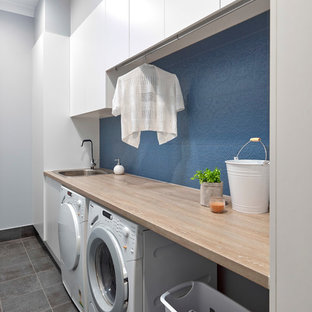 Photo of a small contemporary single-wall separated utility room in Adelaide with a built-in sink, flat-panel cabinets, white cabinets, laminate countertops, blue walls, porcelain flooring, a side by side washer and dryer, grey floors and orange worktops.