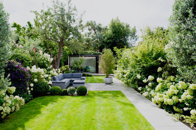Large contemporary back formal full sun garden for summer in London with a flowerbed, natural stone paving and a wood fence.