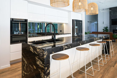 Design ideas for a contemporary galley kitchen in Sunshine Coast with an undermount sink, flat-panel cabinets, white cabinets, window splashback, black appliances, dark hardwood floors, with island, brown floor and black benchtop.
