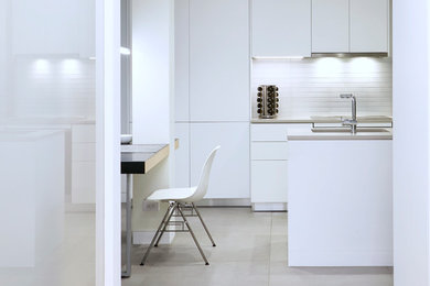 Photo of a small modern u-shaped eat-in kitchen in New York with an undermount sink, flat-panel cabinets, white cabinets, quartz benchtops, white splashback, glass tile splashback, panelled appliances, no island and white benchtop.