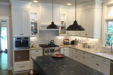 Example of a mid-sized farmhouse l-shaped brown floor enclosed kitchen design in Atlanta with an undermount sink, shaker cabinets, white cabinets, granite countertops, white backsplash, subway tile backsplash, stainless steel appliances, an island and brown countertops