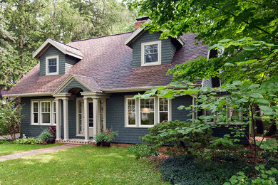 Photo of a mid-sized country two-storey green house exterior in Detroit with wood siding, a clipped gable roof and a shingle roof.