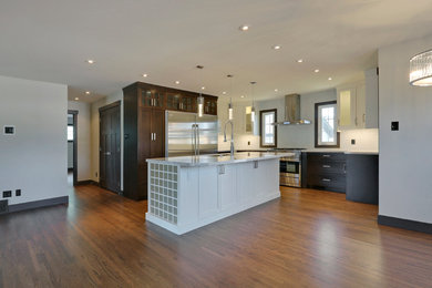 Inspiration for a mid-sized timeless l-shaped light wood floor and brown floor eat-in kitchen remodel in Calgary with an undermount sink, shaker cabinets, dark wood cabinets, granite countertops, white backsplash, stone tile backsplash, stainless steel appliances and an island