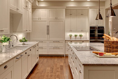 Inspiration for a large transitional l-shaped medium tone wood floor eat-in kitchen remodel in Seattle with an undermount sink, white cabinets, granite countertops, white backsplash, ceramic backsplash, paneled appliances and an island
