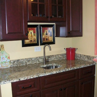 Photo of a mid-sized traditional u-shaped kitchen pantry in Chicago with an undermount sink, raised-panel cabinets, dark wood cabinets, granite benchtops, white splashback, ceramic splashback, white appliances, light hardwood floors, with island, beige floor and yellow benchtop.