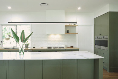 Inspiration for a mid-sized contemporary galley eat-in kitchen in Sunshine Coast with a double-bowl sink, recessed-panel cabinets, green cabinets, quartz benchtops, white splashback, ceramic splashback, stainless steel appliances, vinyl floors, with island, brown floor and white benchtop.