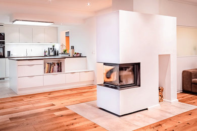 Mittelgroße, Offene Moderne Küche in grau-weiß in U-Form mit braunem Holzboden, braunem Boden, eingelassener Decke, Doppelwaschbecken, flächenbündigen Schrankfronten, weißen Schränken, Mineralwerkstoff-Arbeitsplatte, Küchenrückwand in Weiß, schwarzen Elektrogeräten, Halbinsel, schwarzer Arbeitsplatte und Durchreiche in Sonstige