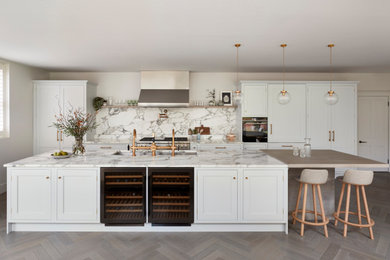 Inspiration for a large traditional grey and white galley open plan kitchen in Hampshire with a built-in sink, shaker cabinets, grey cabinets, marble worktops, white splashback, marble splashback, stainless steel appliances, light hardwood flooring, an island, beige floors, white worktops and feature lighting.