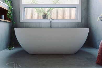 Inspiration for a mid-sized contemporary bathroom in Geelong with a freestanding tub, gray tile, porcelain tile, porcelain floors, a wall-mount sink, solid surface benchtops, grey floor, a hinged shower door and white benchtops.
