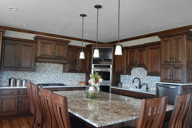 Large traditional l-shaped separate kitchen in Kansas City with an undermount sink, raised-panel cabinets, medium wood cabinets, granite benchtops, beige splashback, mosaic tile splashback, stainless steel appliances, medium hardwood floors, with island and brown floor.