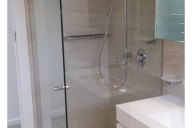 Small modern master bathroom in Sydney with an undermount sink, flat-panel cabinets, white cabinets, glass benchtops, a freestanding tub, a corner shower, a wall-mount toilet, beige tile, porcelain tile, beige walls and porcelain floors.