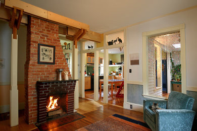 Photo of a mid-sized eclectic enclosed living room in Boston with dark hardwood floors, a standard fireplace, a brick fireplace surround, white walls and no tv.