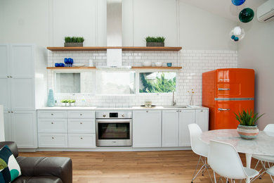 Beach style single-wall open plan kitchen in Other with an undermount sink, shaker cabinets, white cabinets, white splashback, subway tile splashback, coloured appliances, light hardwood floors, no island, beige floor and white benchtop.