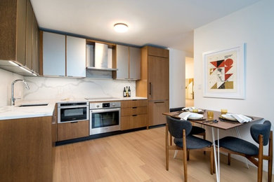 Example of a mid-sized minimalist l-shaped medium tone wood floor and brown floor eat-in kitchen design in New York with an undermount sink, glass-front cabinets, medium tone wood cabinets, marble countertops, white backsplash, marble backsplash, paneled appliances, no island and white countertops