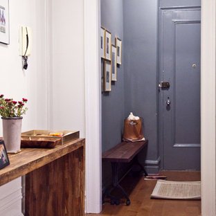 Cette photo montre un hall d'entrée éclectique de taille moyenne avec un mur blanc, un sol en bois brun, une porte simple, une porte grise et un sol marron.