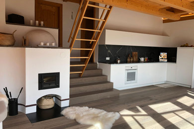 Kleine Wohnküche in L-Form mit Unterbauwaschbecken, weißen Schränken, Granit-Arbeitsplatte, Küchenrückwand in Schwarz, Rückwand aus Granit, weißen Elektrogeräten und dunklem Holzboden in München