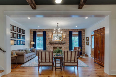 This is an example of a medium sized farmhouse enclosed living room in Nashville with white walls, medium hardwood flooring, a standard fireplace, a brick fireplace surround and no tv.