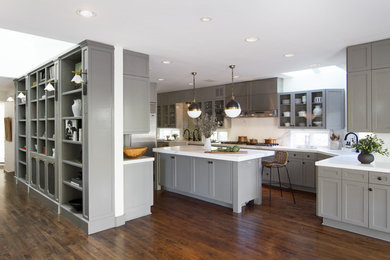 This is an example of a transitional eat-in kitchen in Los Angeles with a farmhouse sink, shaker cabinets, grey cabinets, marble benchtops, white splashback, marble splashback, stainless steel appliances, dark hardwood floors, with island, brown floor and white benchtop.