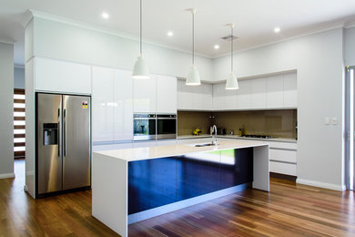 Contemporary kitchen in Perth with an undermount sink, white cabinets, solid surface benchtops, brown splashback, glass sheet splashback, stainless steel appliances, medium hardwood floors and with island.