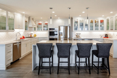 Kitchen - large transitional u-shaped medium tone wood floor and brown floor kitchen idea in Vancouver with an undermount sink, shaker cabinets, white cabinets, quartz countertops, white backsplash, ceramic backsplash, stainless steel appliances, an island and white countertops