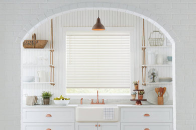 Example of a mid-sized farmhouse single-wall enclosed kitchen design in New York with a farmhouse sink, shaker cabinets, white cabinets, marble countertops, white backsplash, wood backsplash, white appliances and white countertops