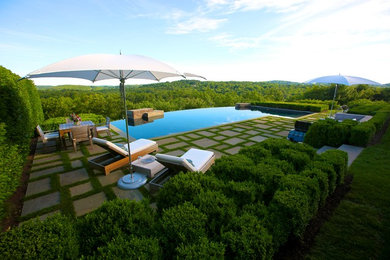 Photo of a large modern backyard custom-shaped infinity pool in New York with a water feature and natural stone pavers.