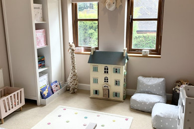 This is an example of a medium sized contemporary toddler’s room for girls in Gloucestershire with pink walls, carpet, beige floors and a vaulted ceiling.