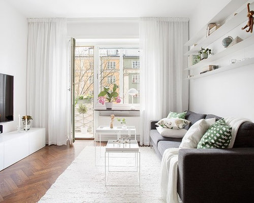 Nordisk inredning av ett separat vardagsrum, med vita väggar, mellanmörkt trägolv, en väggmonterad TV och brunt golv